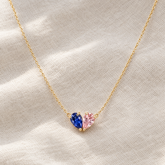 Collier cœur 2 pierres de naissance doré, pierres bleue et rose, posé sur du lin